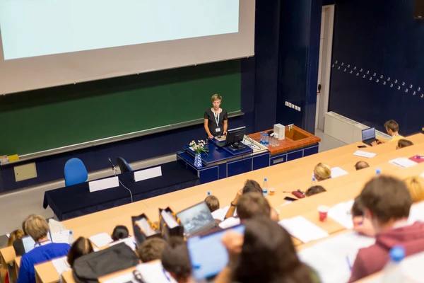 Eine Wissenschaftlerin und ein Wissenschaftler arbeiten hinter einer Glasfassade und mischen Chemikalien mit Großgeräten.